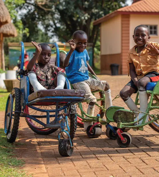 Three young children with leg casts wave from their wheelchairs.