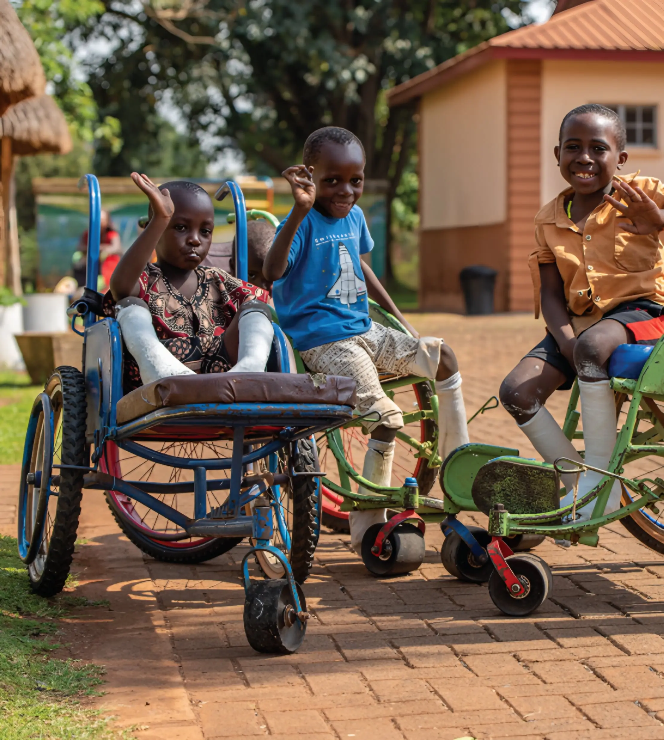 Three young children with leg casts wave from their wheelchairs.
