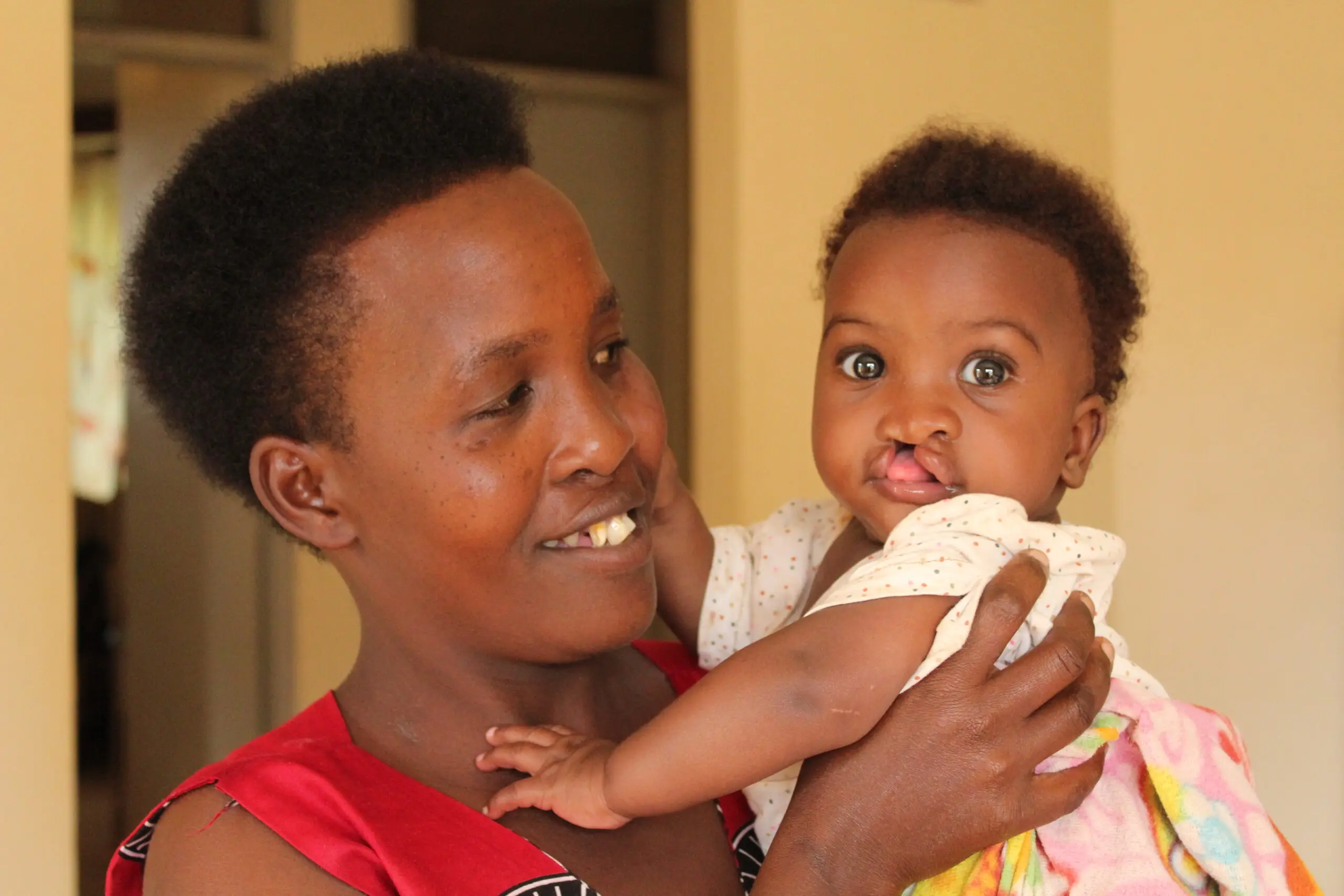 A smiling mother in a red top holds up her baby, who was born with a cleft lip.