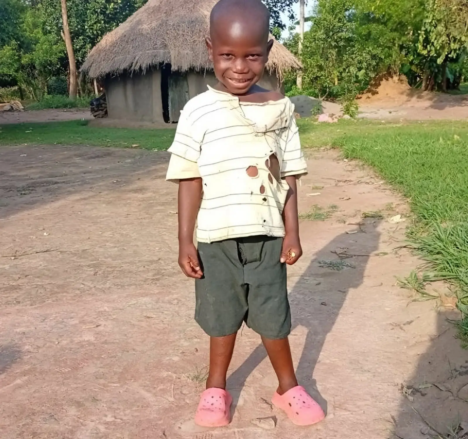 Mark smiles as he stands on a dirt path in front of a thatched house at his grandmother's home.