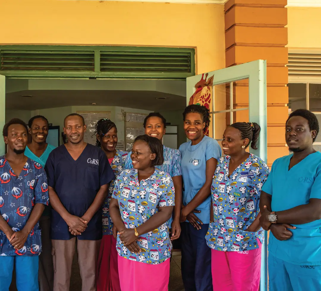 Nurses and clinical staff in colourful scrubs stand smiling in the doorway of a ward.