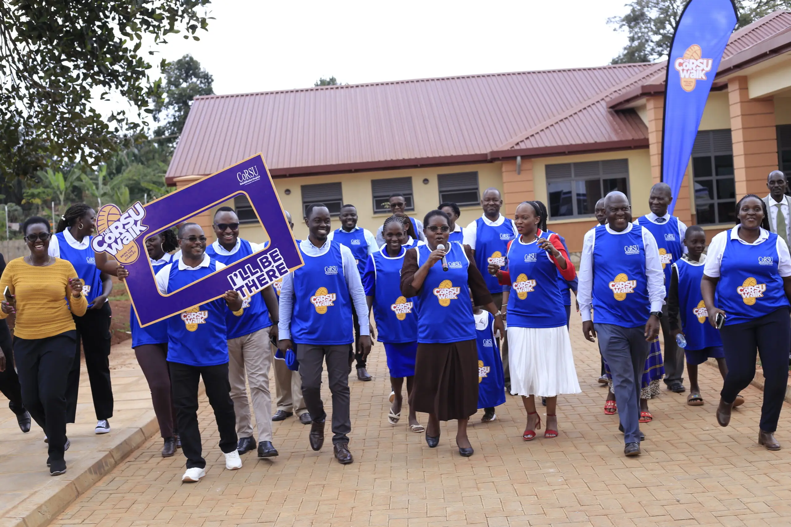 CoRSU staff stride forward together in front of a long red-roofed hospital building.