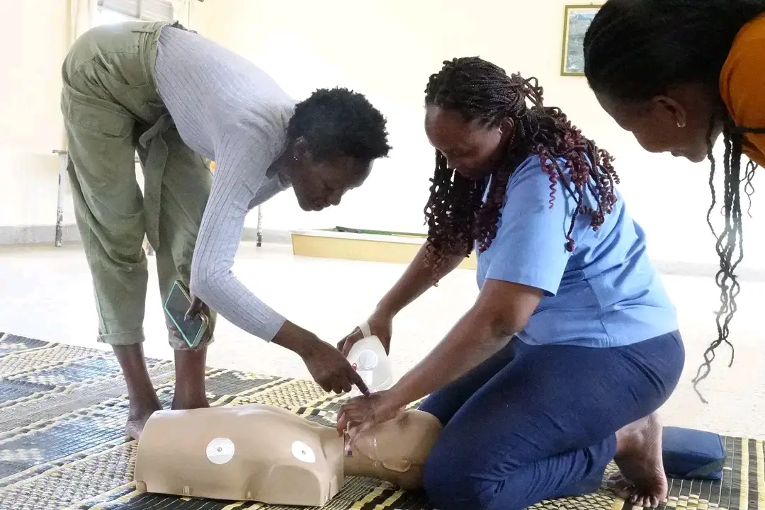 Three nurses bend and kneel around a manikin on a mat during a basic life support practical session.