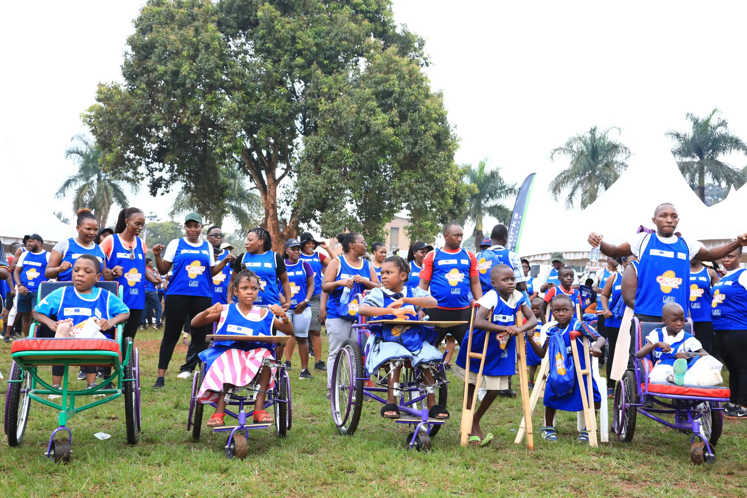 Children in wheelchairs and on crutches line up in front of walkers in blue CoRSU Walk vests.